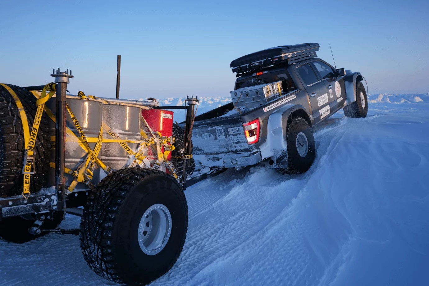 A truck hauls a loaded trailer uphill in the snow.